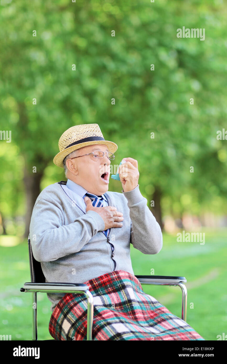 Senior uomo seduto nella sedia di trattenimento di un inalatore e avente un attacco d' asma Foto Stock