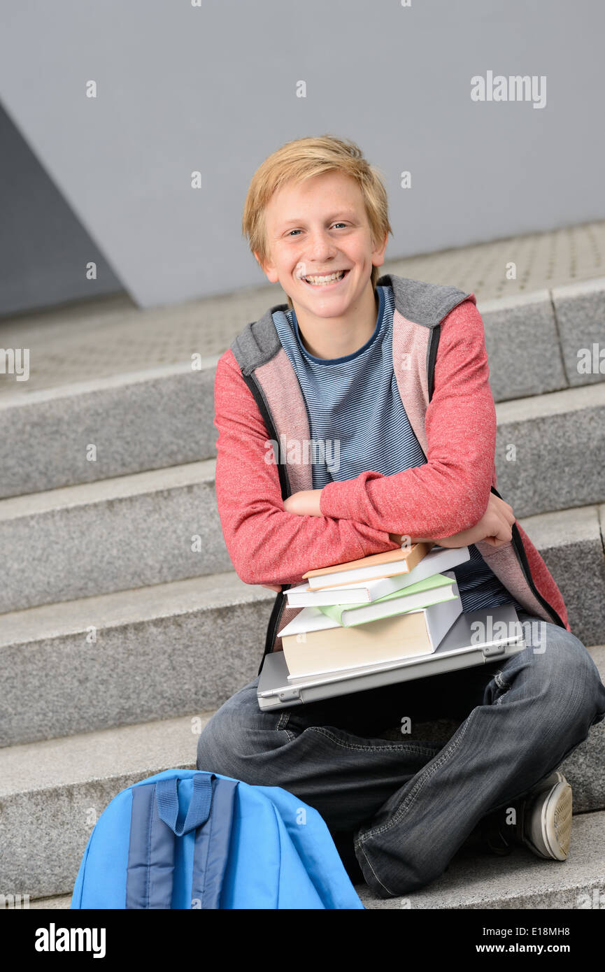 Felice studente con libri e computer portatile al di fuori seduta sui gradini Foto Stock