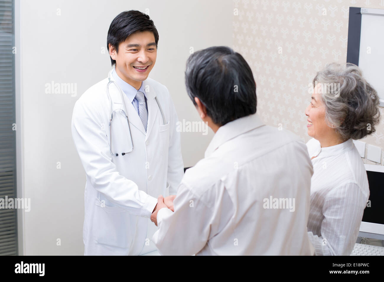 Coppia senior stringono le mani con medico in ospedale Foto Stock