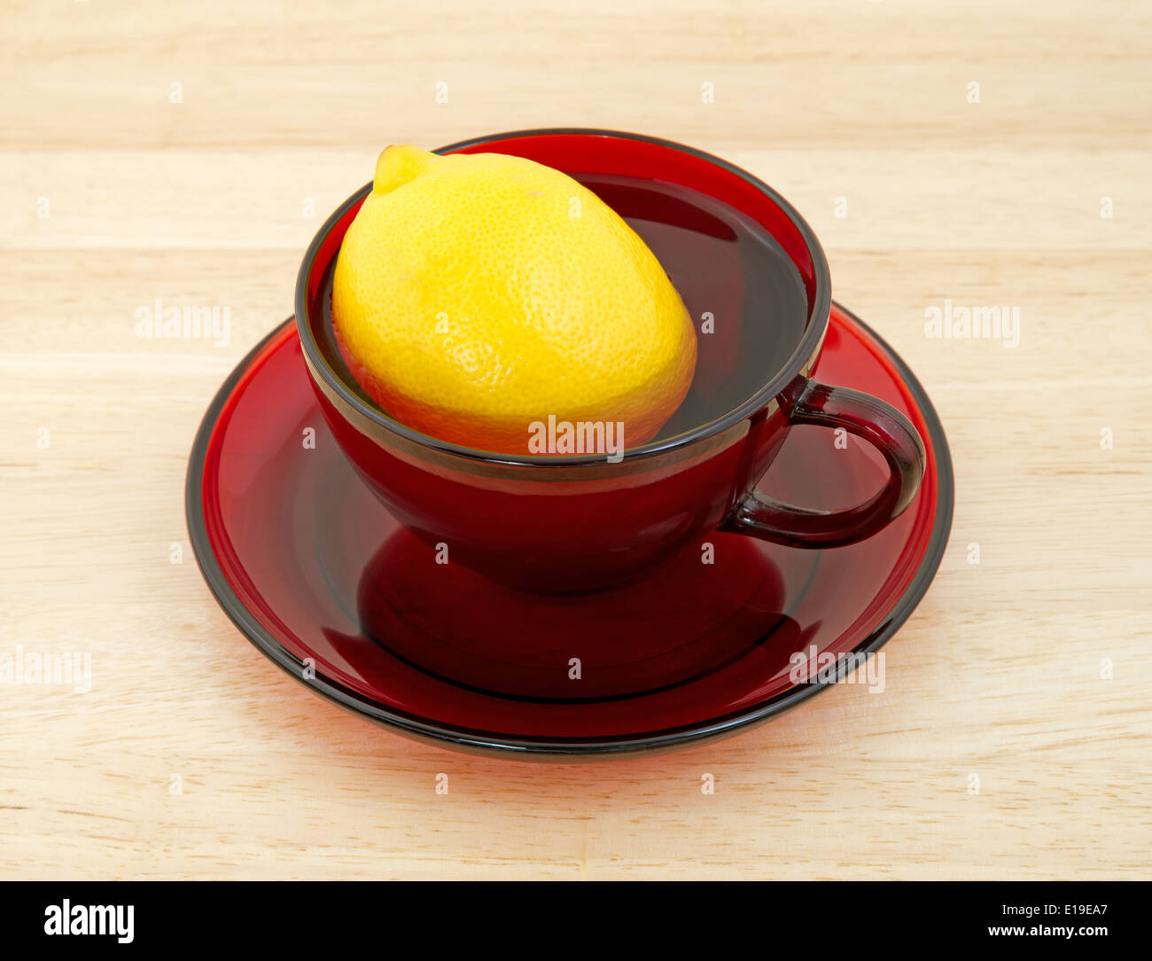 Un grande limone fresco in un bicchiere di rosso e piattino riempiti con acqua in cima a un contatore di legno top a significare una sana combinazione. Foto Stock