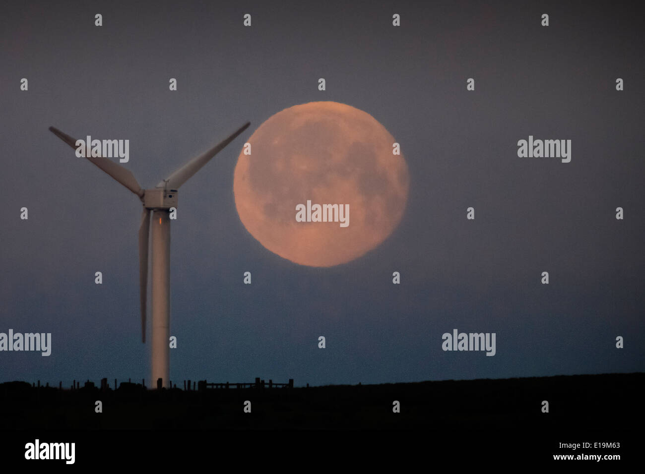 Una luna piena impostazione dietro le turbine eoliche sulla Ovenden Moor vicino a Halifax. Foto Stock
