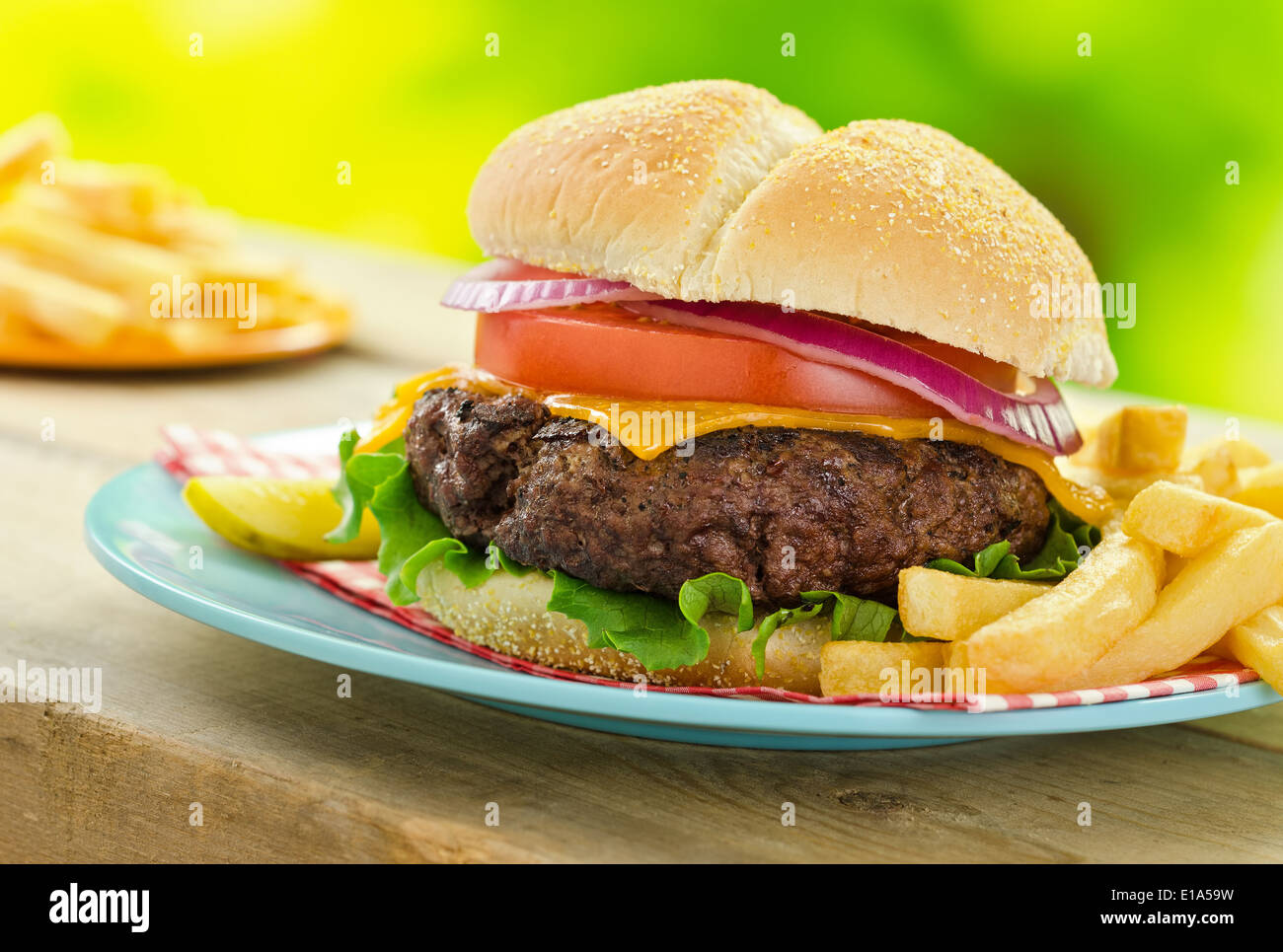 Una deliziosa grigliata di cheeseburger e patatine fritte in un picnic esterno barbecue impostazione. Foto Stock
