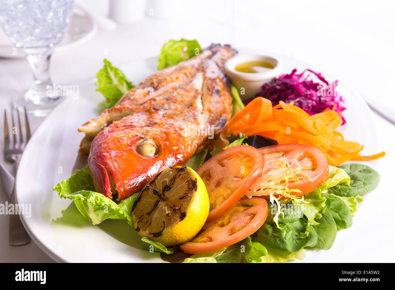 Cucinata tilapia pesce servite in una piastra con verdure e salsa di pesce complimentato con acqua ghiacciata Foto Stock