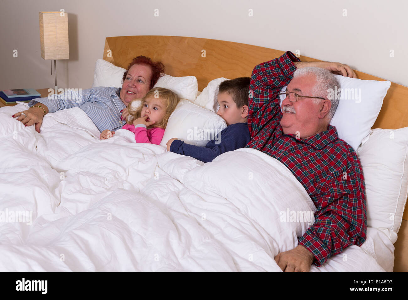Nonni guardando la TV nel letto con loro grand kids, sembrano entusiasti, forse il suo un film d'avventura Foto Stock