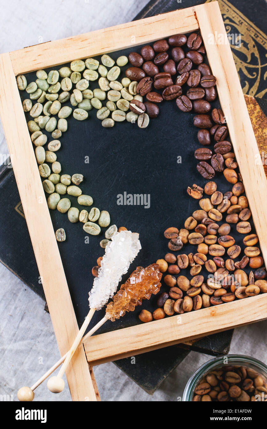 Verde, marrone caffè decaffeinato non torrefatto e nero caffè in grani con bastoncini di zucchero su Nero lavagna vuota su libri vintage. Vista dall'alto. Foto Stock