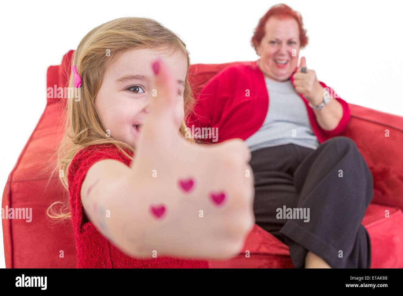 Carino bambina con cuore rosso dipinto sulla sua mano dando un pollice in alto gesto di approvazione con sua nonna che è seduto o Foto Stock