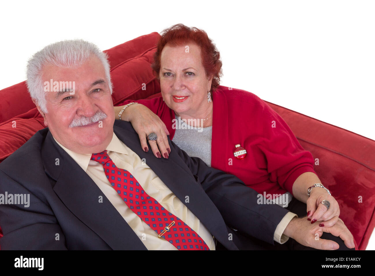 Elevato angolo di visione di un attraente ed elegante coppia senior seduti insieme su un divano rosso guardando verso l'alto la fotocamera con cordiale Foto Stock