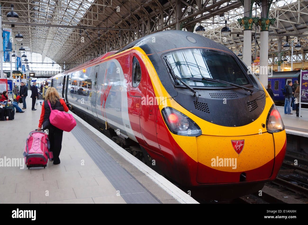 Signora a piedi passeggero sulla piattaforma con i bagagli alla Vergine treno pendolino a Manchester Piccadilly Station; donna con valigia rosa; bagagli Foto Stock