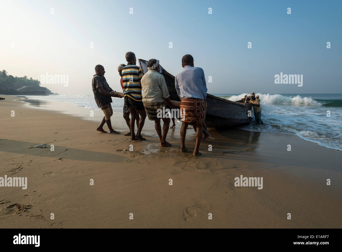 I pescatori tirando una barca sulla spiaggia, Varkala Kerala, India Foto Stock