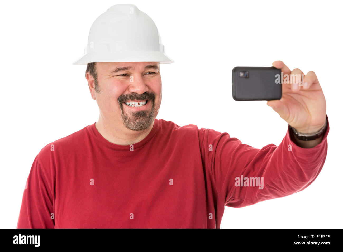 Workman con un bel pizzetto barba lo svezzamento un hardhat posa per un autoritratto dando una cheesy grin come egli guarda nella telecamera o Foto Stock