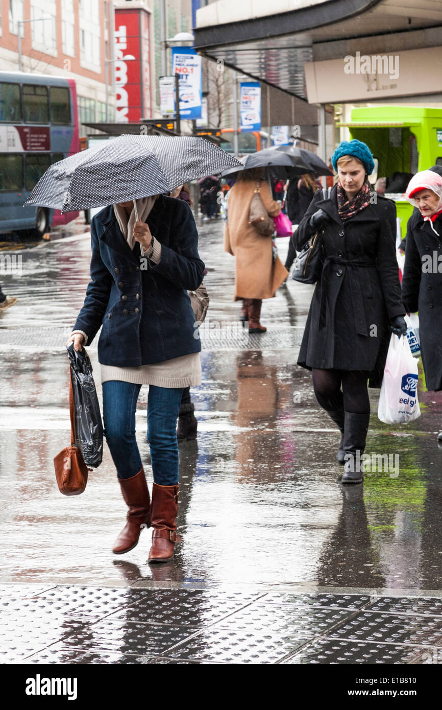 Piove, città del Regno Unito. Donna con ombrello fino e altre persone fuori shopping e attraversando la strada sotto la pioggia, Nottingham, Inghilterra, Regno Unito Foto Stock