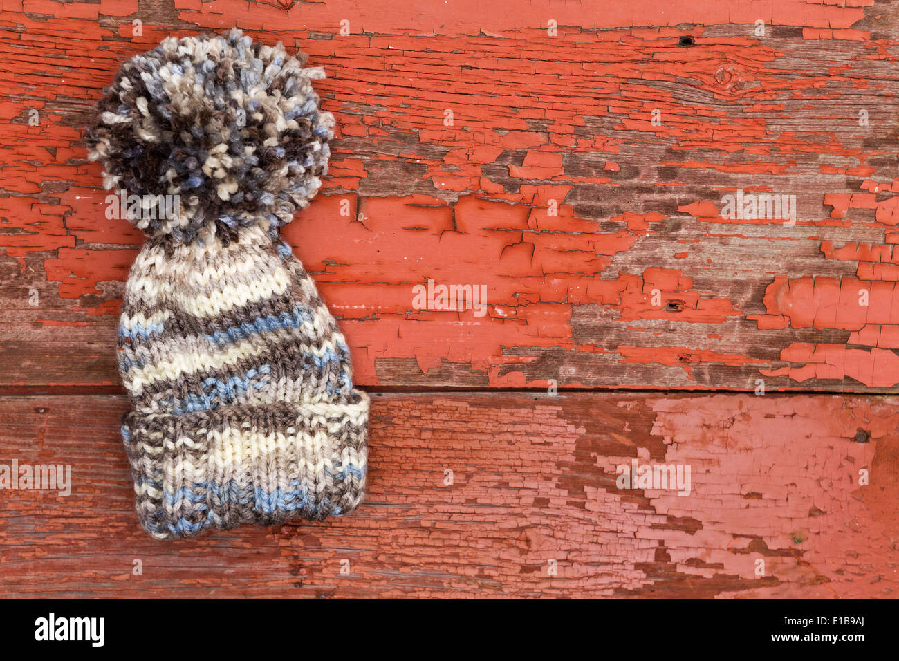 Carino caldo inverno lana hat con un grande pompom giacente su un vecchio legno Tavolo picnic con un grungy superficie di peeling vernice rossa Foto Stock
