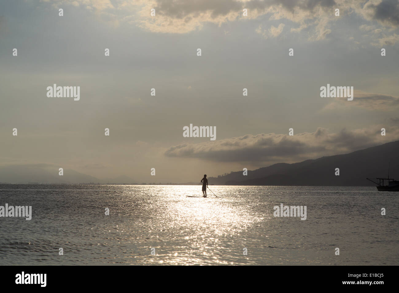 Un uomo practice stand up paddle durante il tramonto nel canto Spiaggia Grande, Bombinhas. Santa Catarina, Brasile Foto Stock