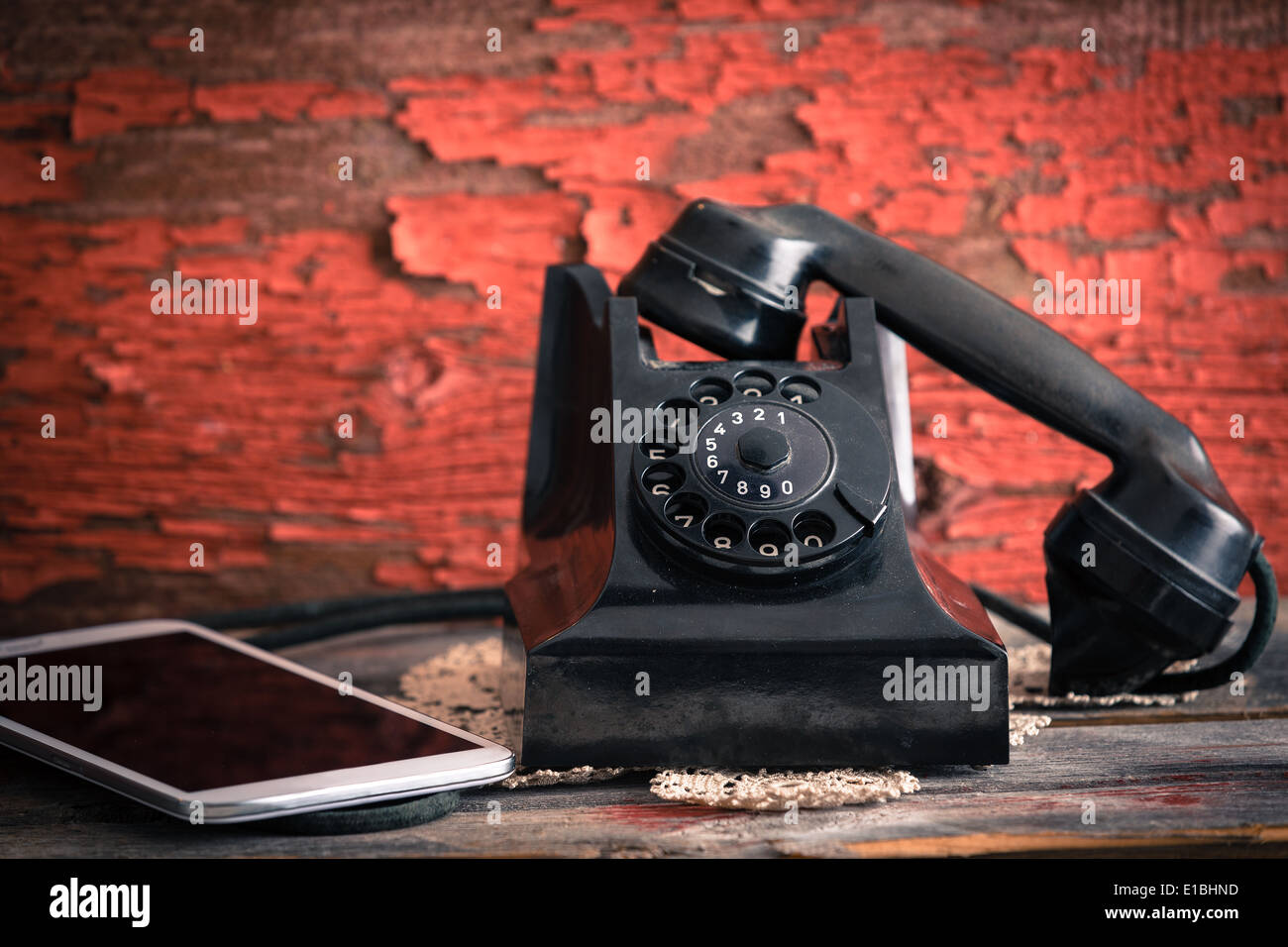 Vecchio telefono rotante con il ricevitore sganciato accanto a un computer tablet che mostra il vecchio stile e moderne forme di co Foto Stock