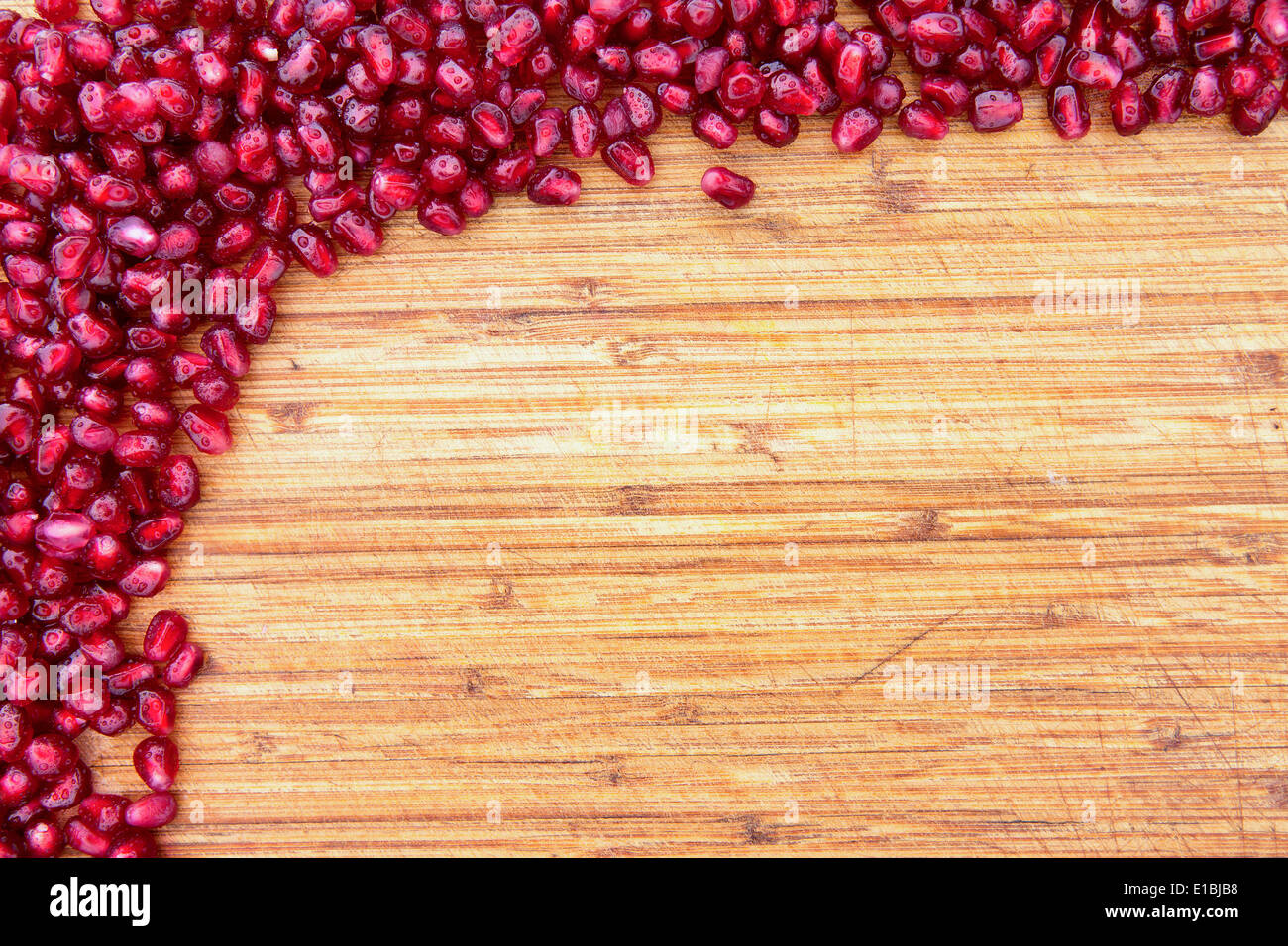 Confine di freschi maturi rosso semi di melograno su una texture di sfondo di legno disposte in una pila nell'angolo in alto a sinistra con ampio cop Foto Stock