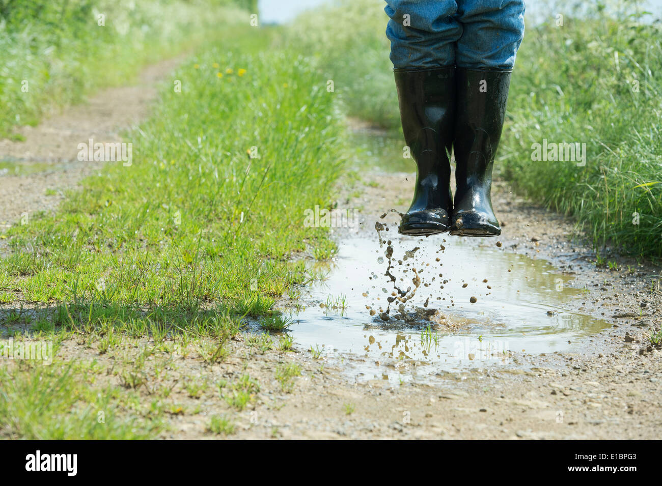Uomo in stivali da pioggia saltando in una pozza d'acqua su una traccia nella campagna inglese Foto Stock