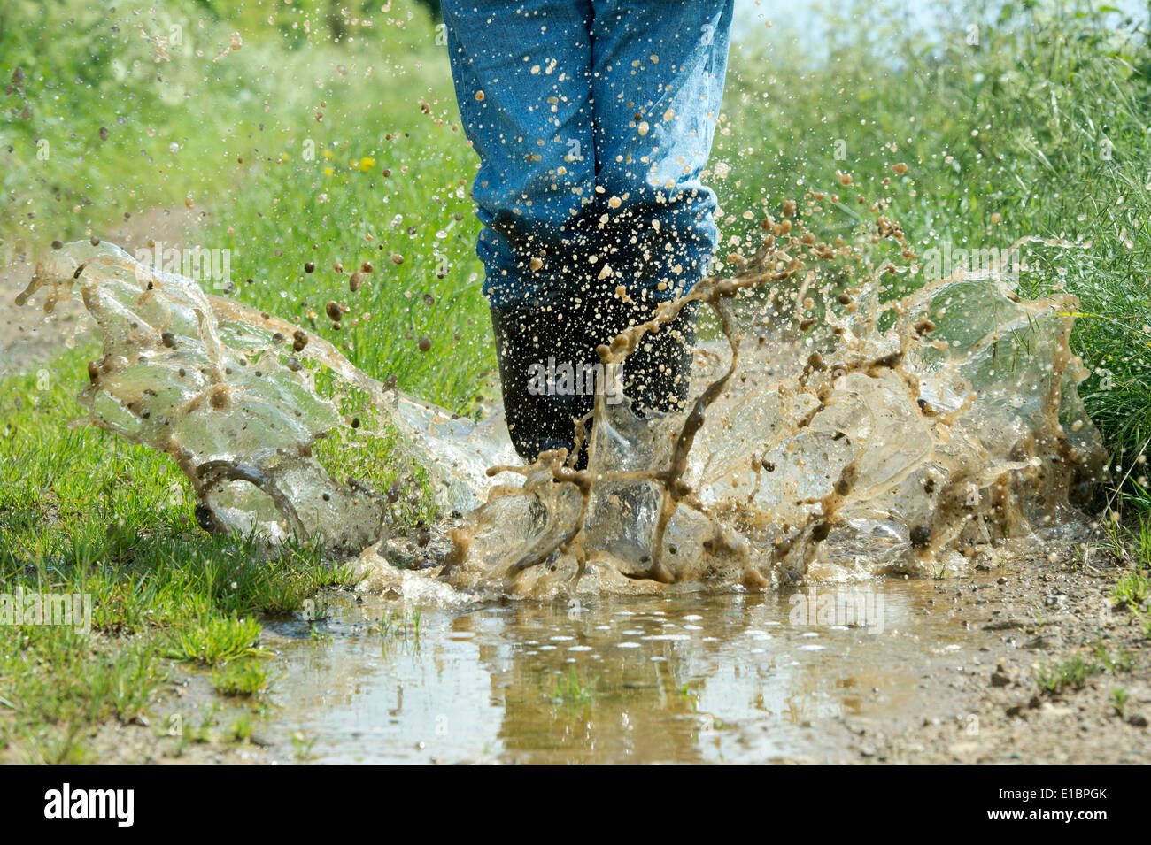 Uomo in stivali da pioggia saltando in una pozza d'acqua su una traccia nella campagna inglese Foto Stock