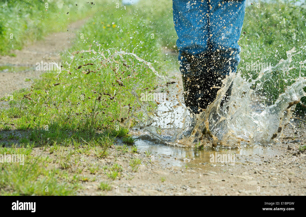 Uomo in stivali da pioggia saltando in una pozza d'acqua su una traccia nella campagna inglese Foto Stock