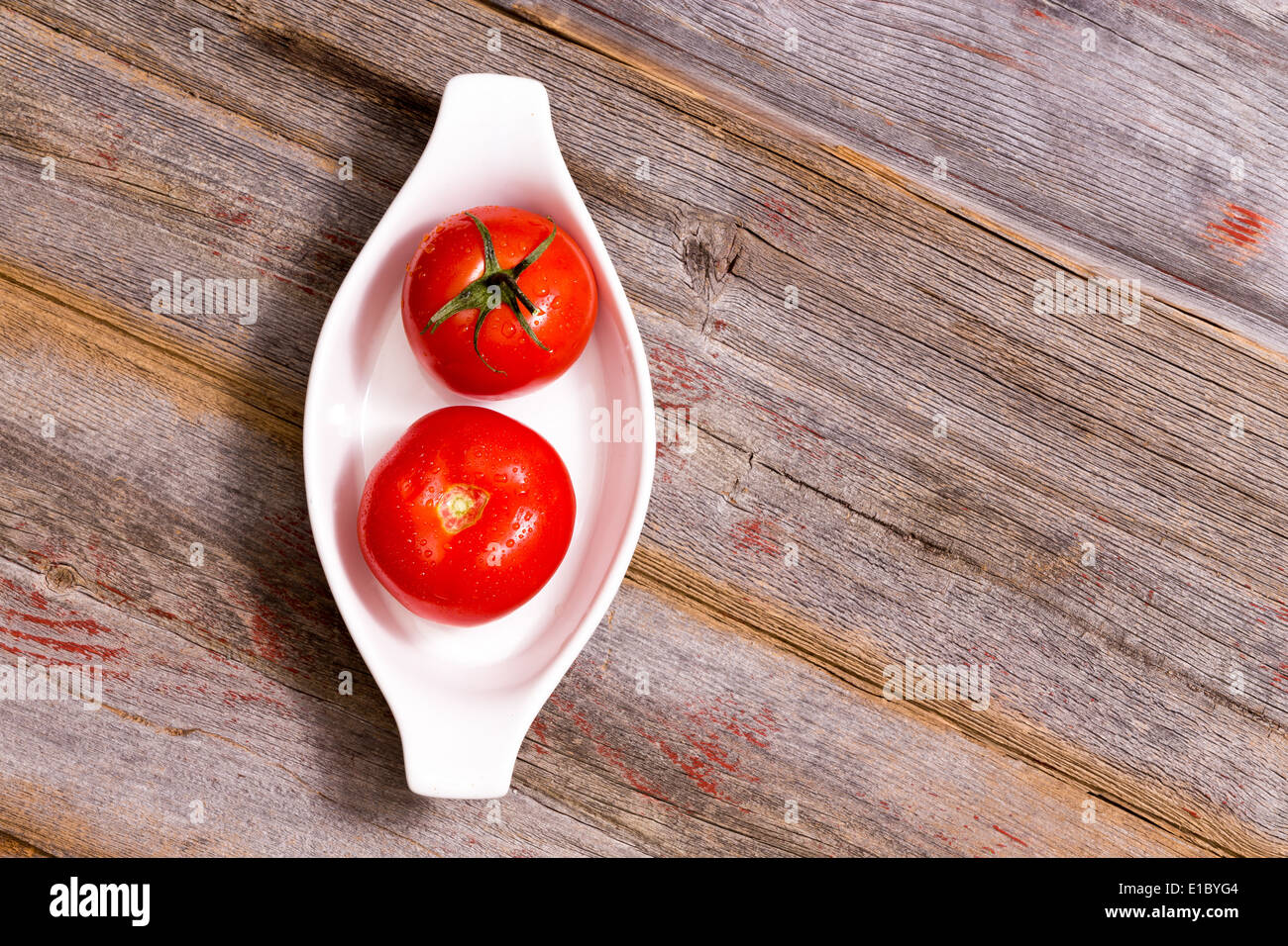 Due succosa mature pomodori rossi in una piccola bianca piatto in ceramica disposti in modo tale che il peduncolo verde è più in alto su uno e rimosso su th Foto Stock