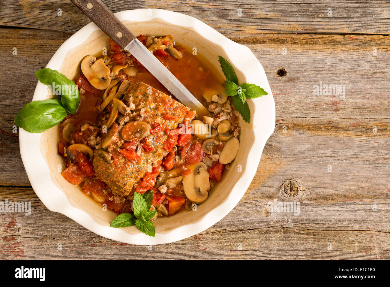 Tagliate a fette polpettone saporito con funghi e verdure servita in una casseruola su una tavola in legno rustico con grungy peeling dolore rosso Foto Stock