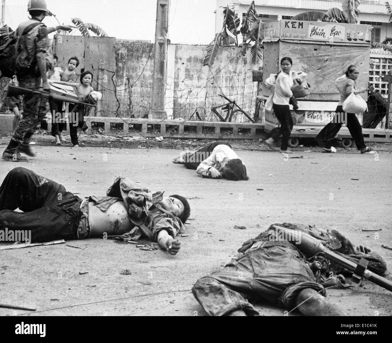 Guerra del Vietnam, le donne e i bambini caricato verso il basso con salvataggio e possedimenti scurry passato i corpi dei tre Viet Cong ucciso Foto Stock