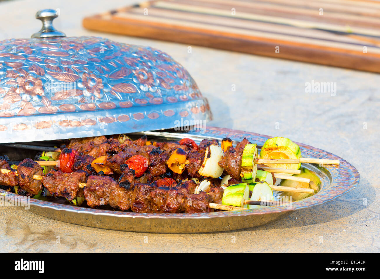 Gustose grigliate di carne di manzo e verdure spiedini su piastra in metallo con apertura coperchio a cupola sul contatore di calcestruzzo all'aperto, in una cucina estiva Foto Stock