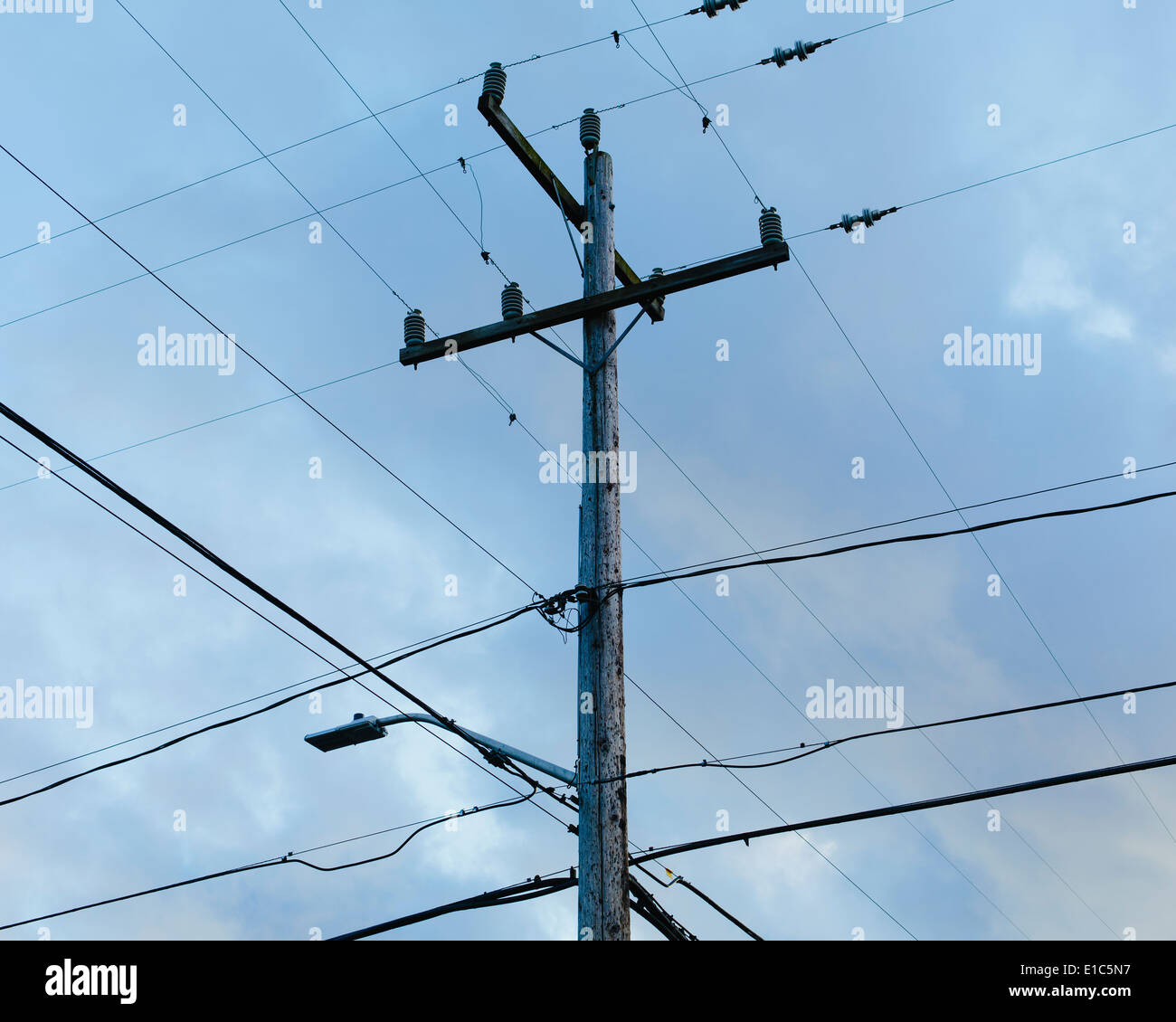 Palo telefonico e linee di alimentazione elettrica osservato dalla terra, contro un cielo nuvoloso. Foto Stock