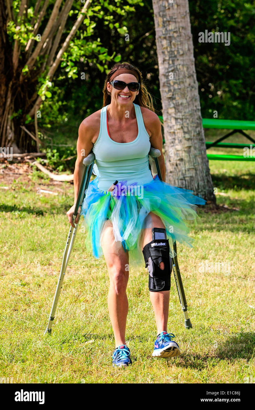 Donna che indossa un tutore per ginocchio e usando stampelle a un empio Tu-Tu evento Foto Stock