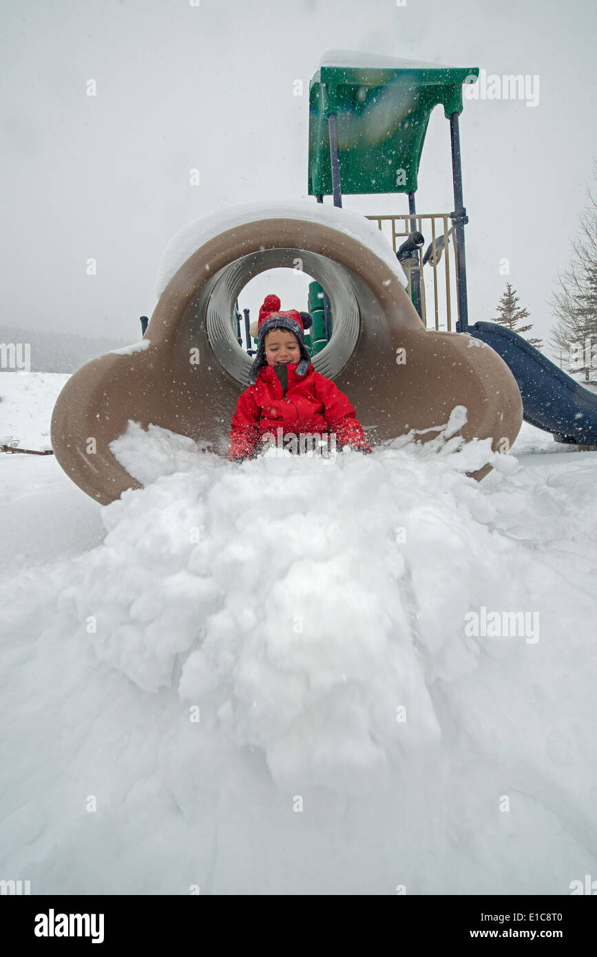 Un 6-anno-vecchio ragazzo scorre su terreni innevati parco giochi. Foto Stock