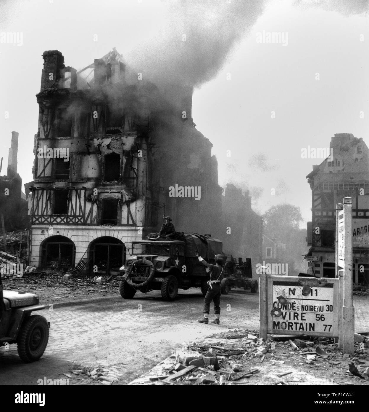 Soldato canadese controlli il traffico nella masterizzazione Falaise rovine il 17 agosto 1944. Un carrello traino di un anti-aerei pistola aziona Foto Stock