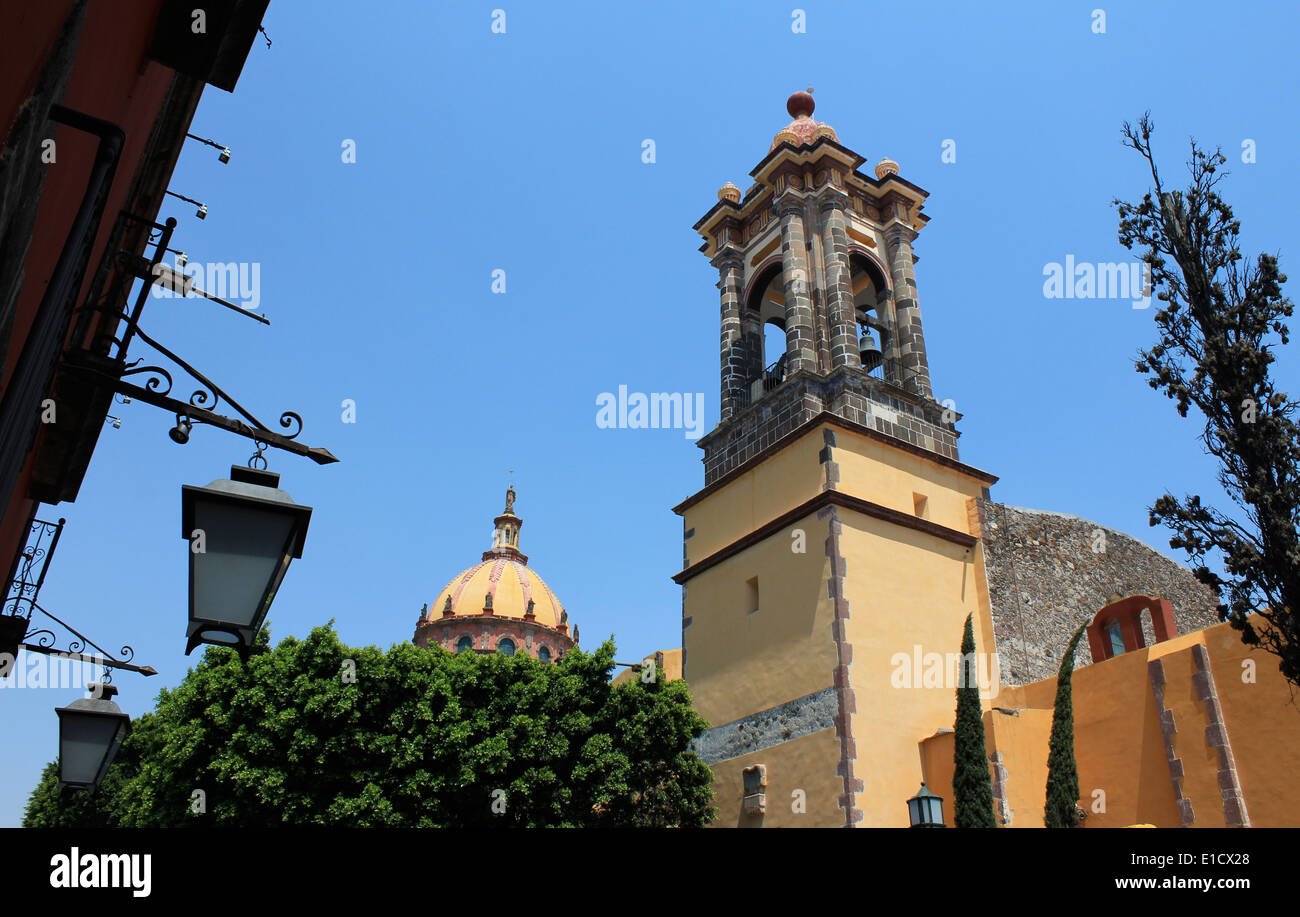 Giallo chiesa con campanile e cupola vista dalla strada con una lampada overhead, San Miguel De Allende, Guanajuato, Mexic Foto Stock