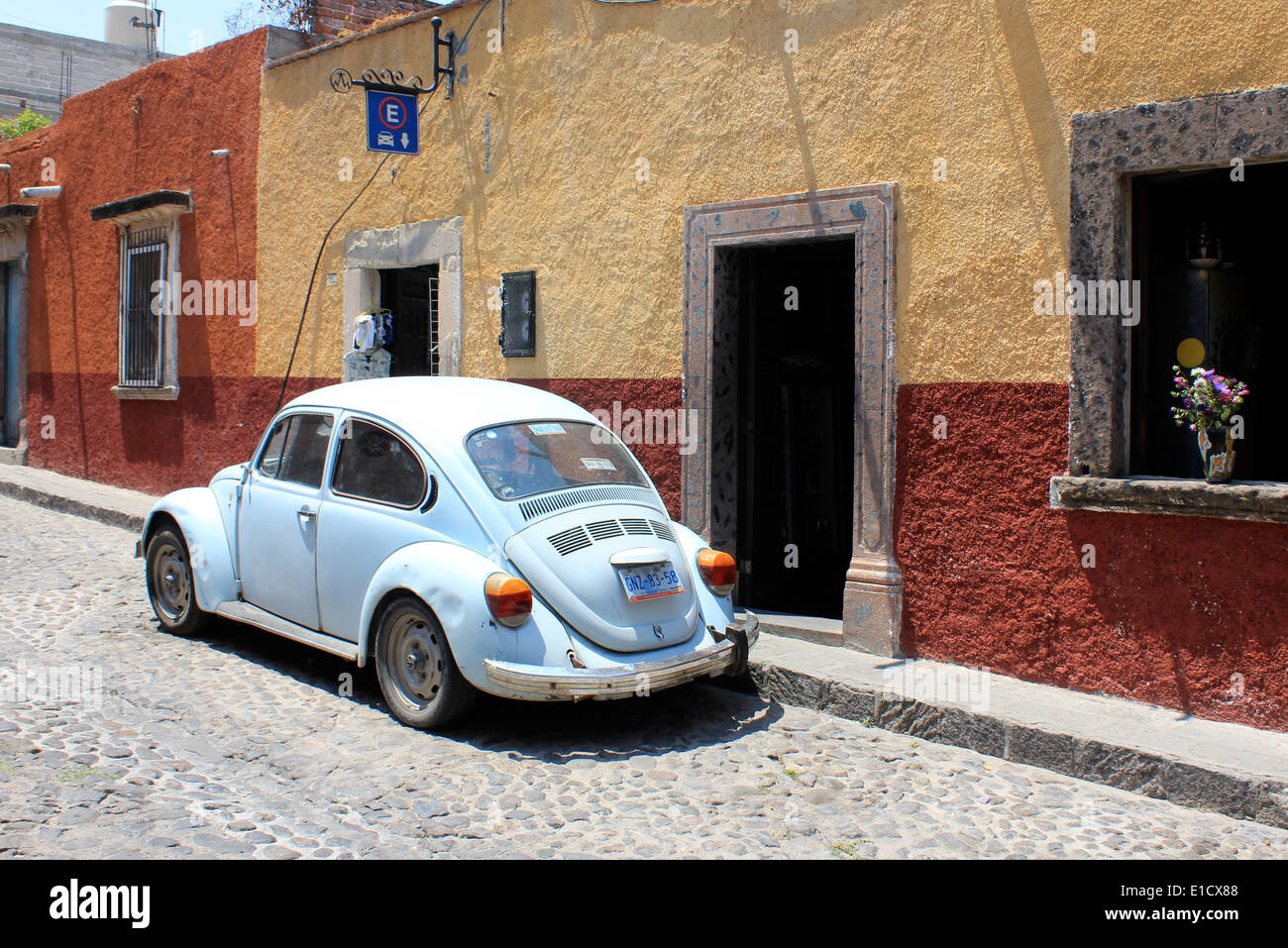 Auto blu chiaro VW Beetle o vocho messicano fuori tipiche case coloniali colorate lungo la strada acciottolata a San Miguel de Allende, Guanajuato, Messico Foto Stock
