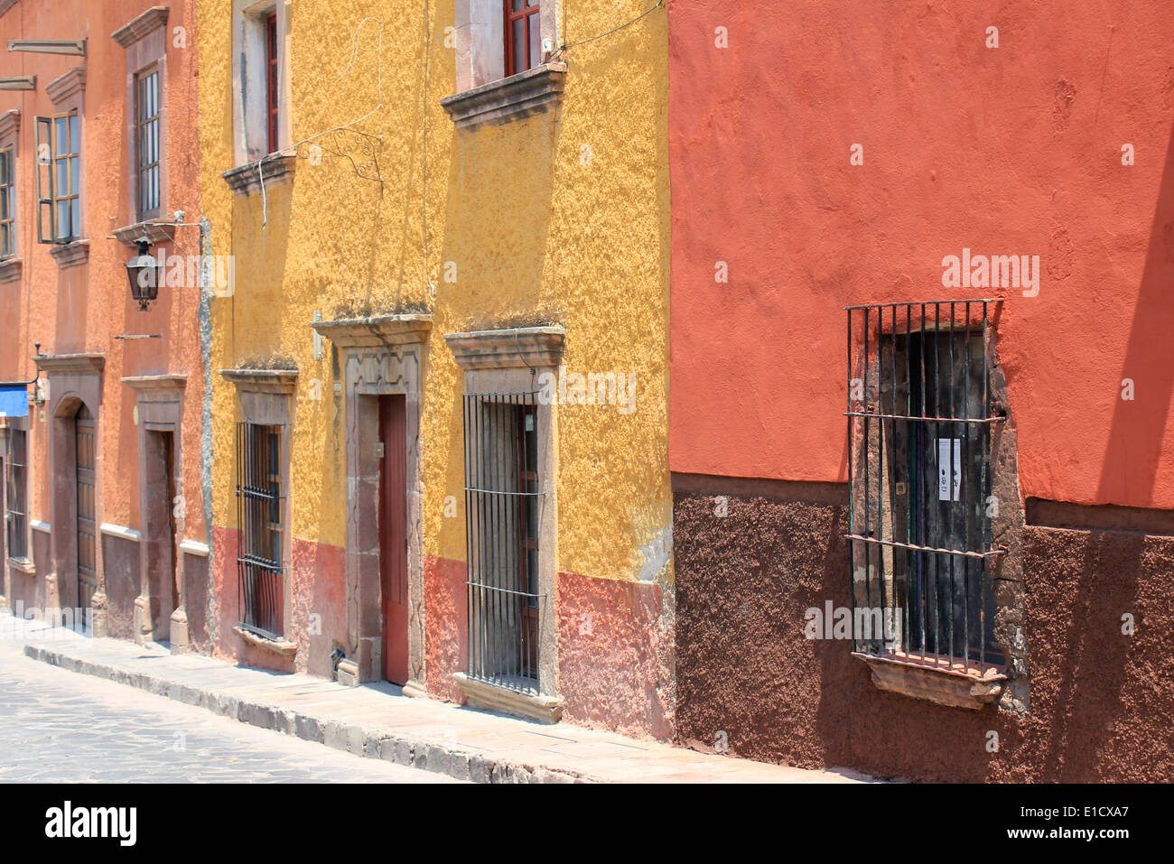 Case coloniali di colore rosso, giallo e arancione che costeggiano una strada a San Miguel de Allende, Guanajuato, Messico Foto Stock