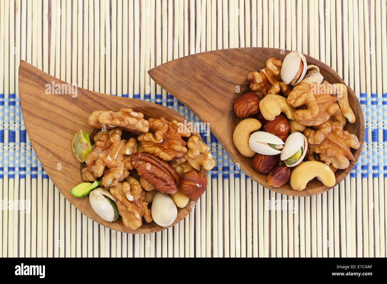 Selezione di dadi misti in ciotole di legno sul tappetino di bambù Foto Stock