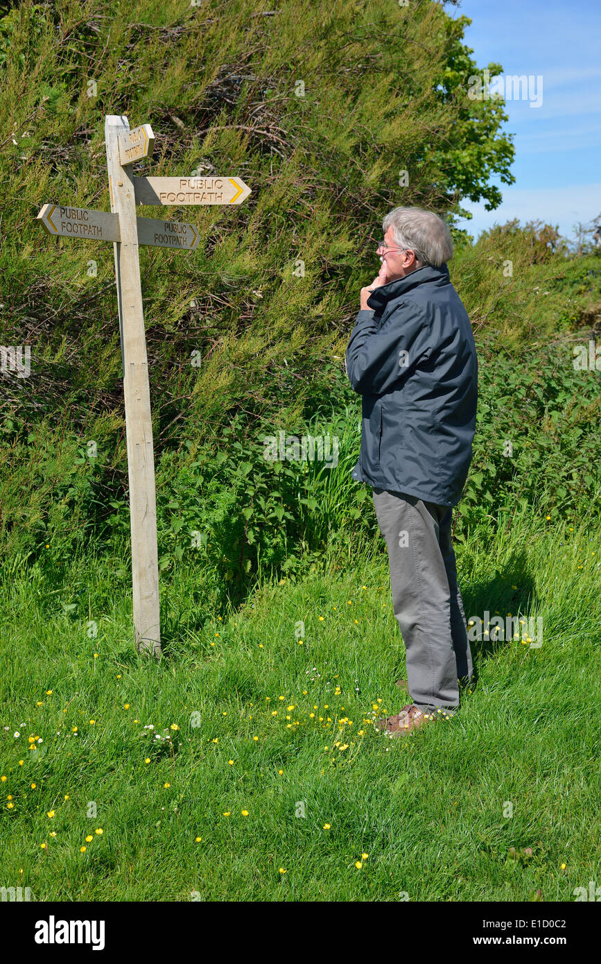 L'uomo fa una scelta di direzione in piedi accanto a un pubblico di legno foothpath signpost dito (post) a Snow Hill, West Wittering, West Sussex, Regno Unito Foto Stock