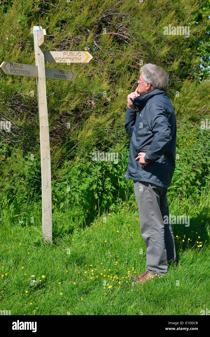 L'uomo fa una scelta di direzione in piedi accanto a un pubblico di legno foothpath signpost dito (post) a Snow Hill, West Wittering, West Sussex, Regno Unito Foto Stock