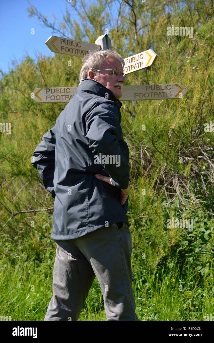 L'uomo fa una scelta di direzione in piedi accanto a un pubblico di legno foothpath signpost dito (post) a Snow Hill, West Wittering, West Sussex, Regno Unito Foto Stock