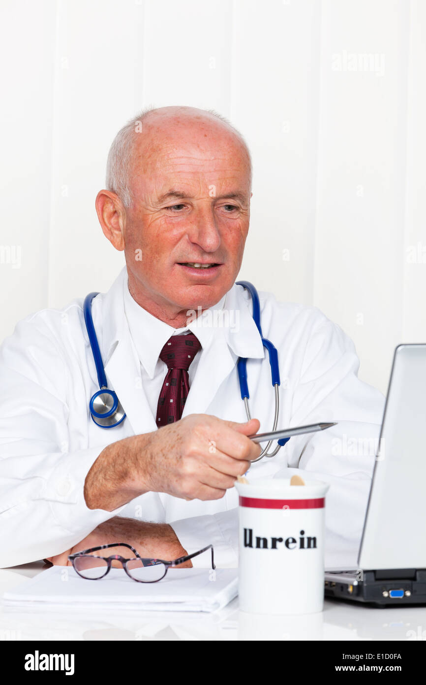 Un medico nella sua pratica medica con uno stetoscopio e laptop. Foto Stock