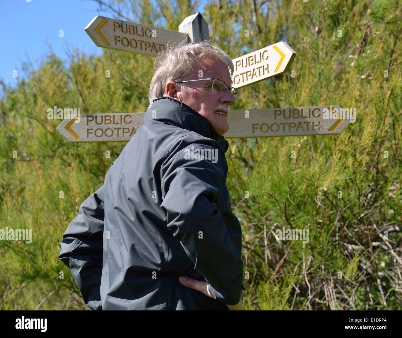 L'uomo fa una scelta di direzione in piedi accanto a un pubblico foothpath segno a Snow Hill, West Wittering, West Sussex, Regno Unito Foto Stock