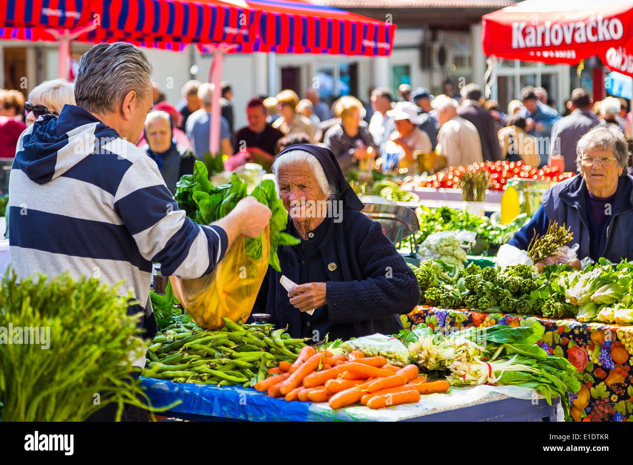 Una donna che vende le verdure fresche dal suo stallo a il mercato giornaliero in Split Croazia Foto Stock