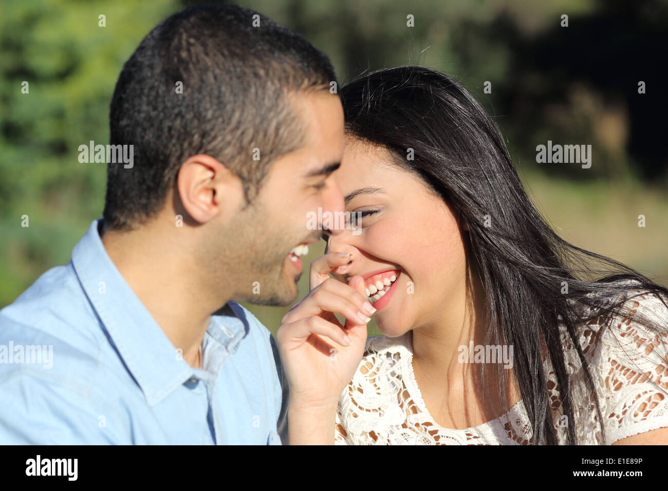 Arab casual giovane uomo e donna flirtare e ridere felici in un parco con uno sfondo verde Foto Stock