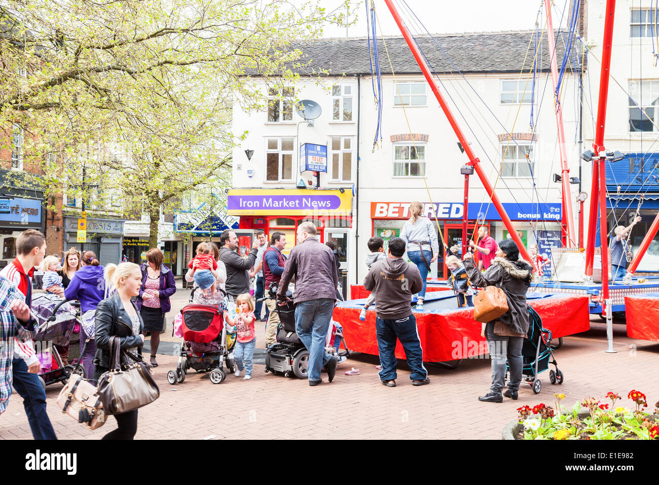 I genitori di scattare le foto e ridere, chat, come i loro figli giocare su bungee swing in centro città di Newcastle Under Lyme. Foto Stock