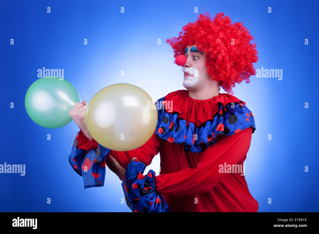 Clown con due palloncini in mano su sfondo blu. Studio di illuminazione professionale Foto Stock
