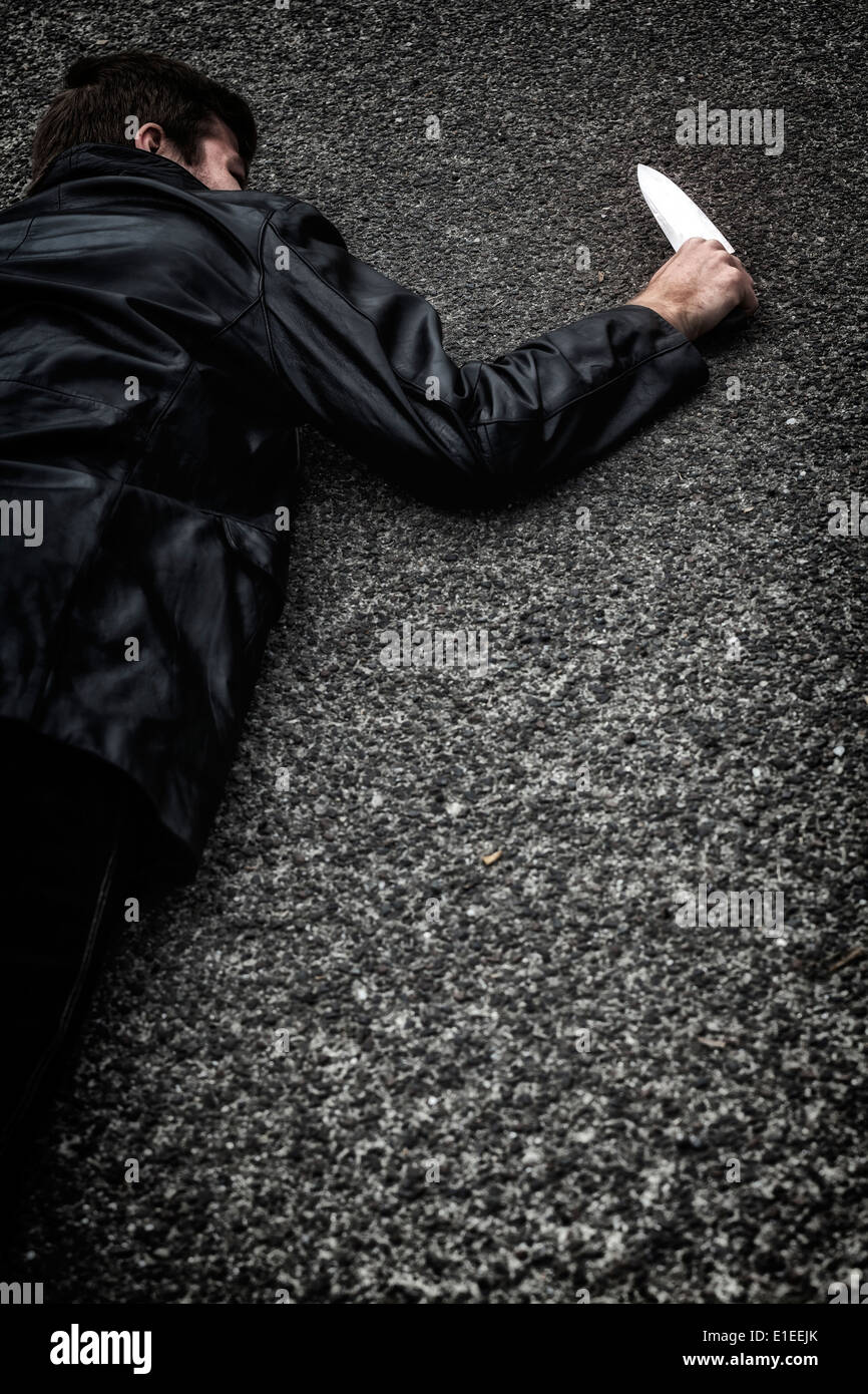 Un uomo con un coltello, giacente sulla strada Foto Stock