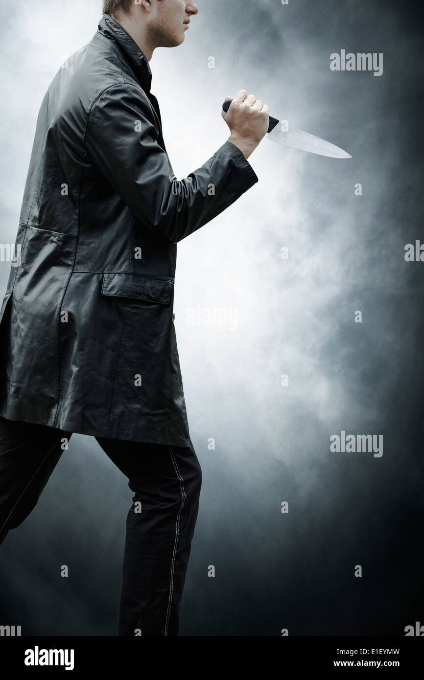 Un uomo in abiti scuri con un coltello Foto Stock