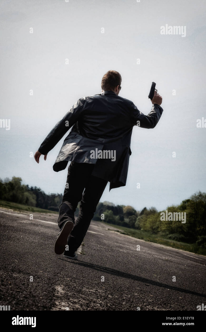 Un uomo che corre su una strada abbandonata con una pistola Foto Stock