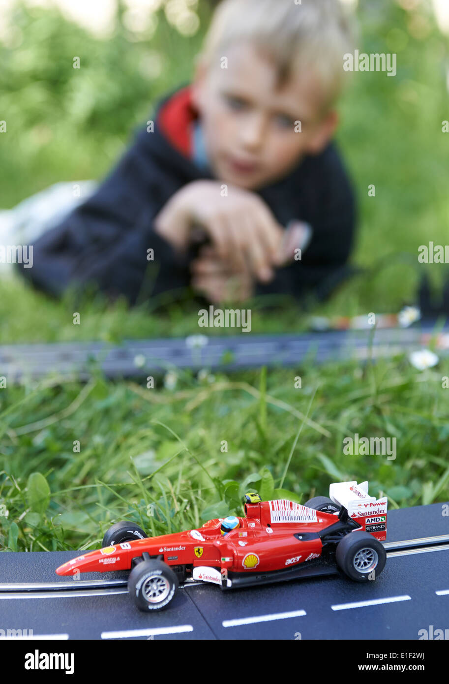 Bambino biondo ragazzo giocando con pista slot car fuori nel prato verde Foto Stock