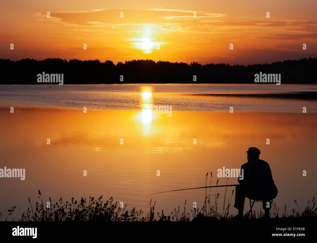 Silhouette di un vecchio pescatore con una canna da pesca di fronte ad un lago e un sole dorato. Meditazione. Vai a pesca! Foto Stock