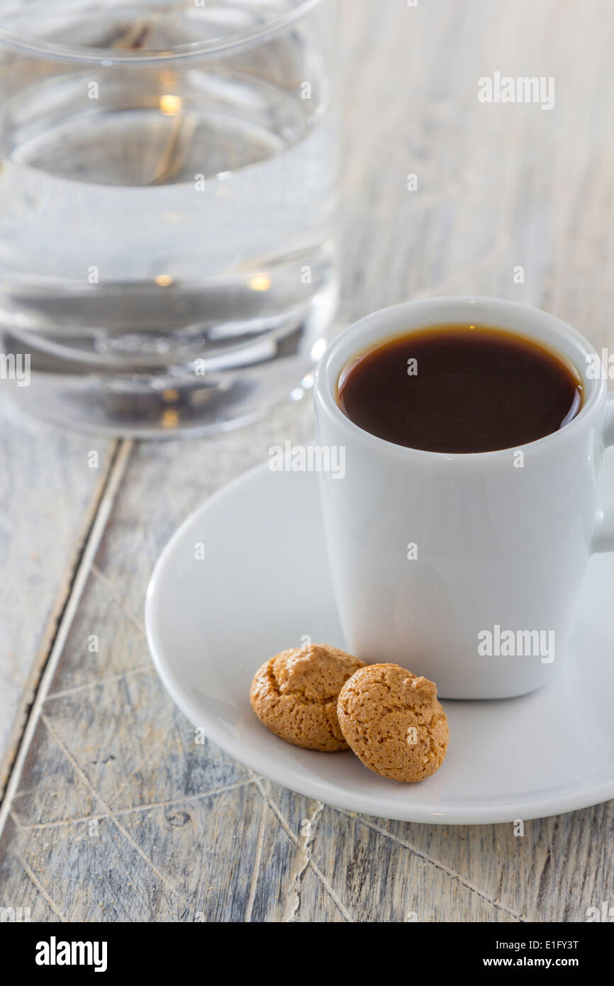 Una tazza di caffè espresso con amarettini italiano i cookie su un tavolo di legno. Tradizionalmente servita con un bicchiere d'acqua. Foto Stock