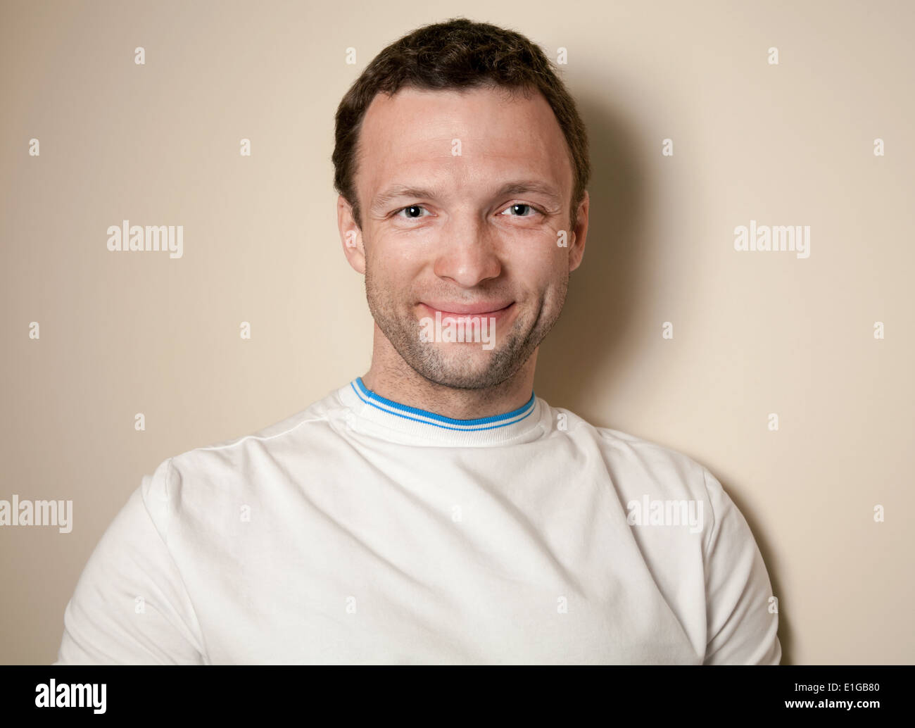 Sorridente giovane uomo caucasico in t-shirt bianco sopra la parete grigia Foto Stock